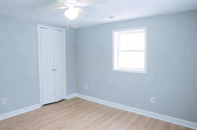 unfurnished bedroom with ceiling fan, light wood-type flooring, a textured ceiling, and a closet