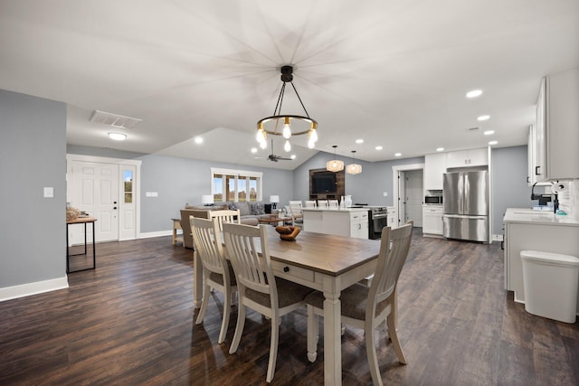 dining space with sink, ceiling fan with notable chandelier, dark wood-type flooring, and lofted ceiling