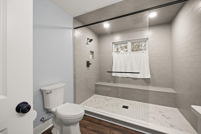 bathroom with tiled shower, wood-type flooring, and toilet