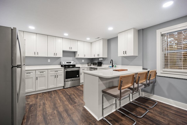 kitchen with kitchen peninsula, appliances with stainless steel finishes, white cabinetry, and dark wood-type flooring