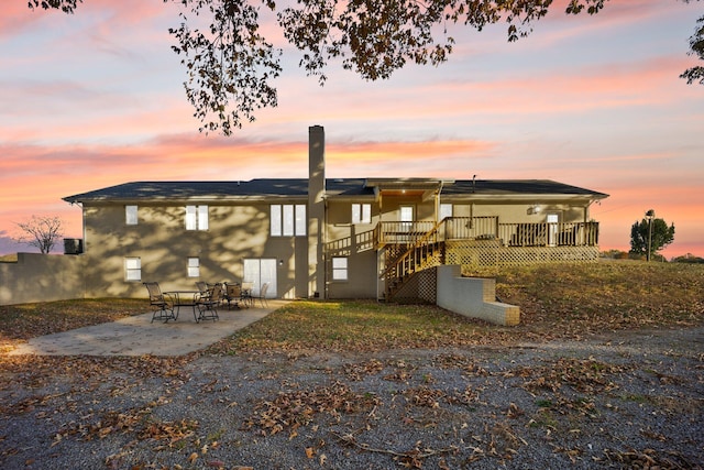 back house at dusk featuring a wooden deck and a patio