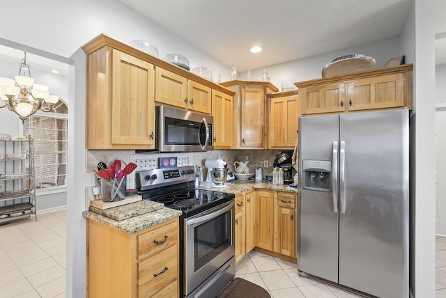 kitchen featuring light stone countertops, appliances with stainless steel finishes, tasteful backsplash, an inviting chandelier, and light tile patterned flooring