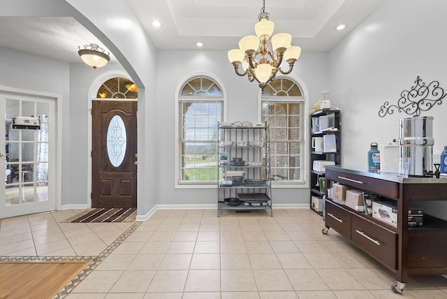 foyer with a tray ceiling, light tile patterned floors, and an inviting chandelier