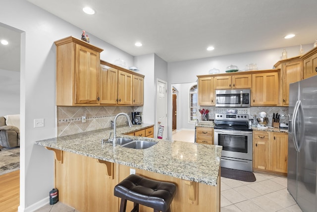 kitchen with sink, decorative backsplash, appliances with stainless steel finishes, a kitchen bar, and kitchen peninsula