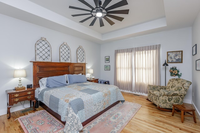 bedroom with ceiling fan, a raised ceiling, and light hardwood / wood-style flooring