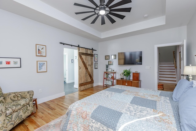 bedroom with ceiling fan, a barn door, a raised ceiling, and wood-type flooring