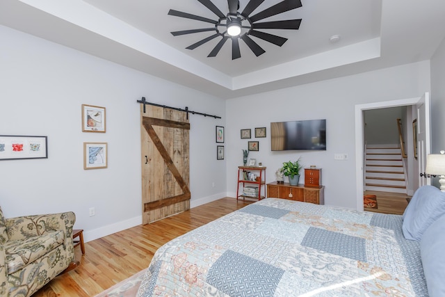 bedroom featuring a tray ceiling, a barn door, ceiling fan, and wood-type flooring