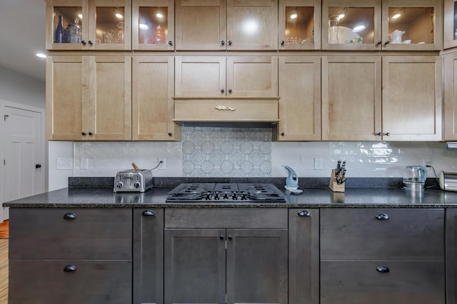 kitchen featuring decorative backsplash, stainless steel gas stovetop, and dark stone counters