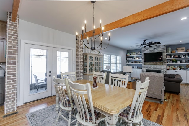 dining space with beamed ceiling, ceiling fan with notable chandelier, light hardwood / wood-style floors, and a brick fireplace