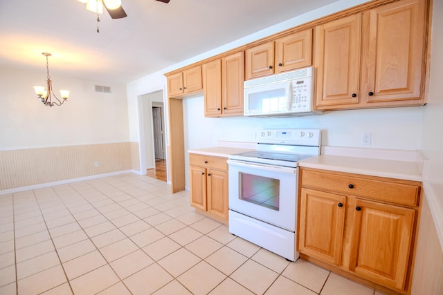 kitchen with wood walls, white appliances, hanging light fixtures, light tile patterned floors, and ceiling fan with notable chandelier