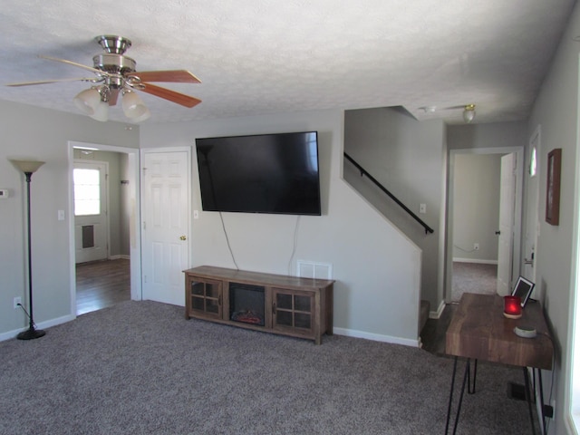 carpeted living room featuring ceiling fan and a textured ceiling