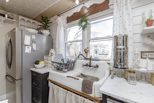 kitchen with stainless steel refrigerator, light stone counters, and a textured ceiling