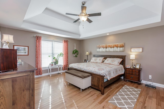 bedroom with ceiling fan, a tray ceiling, and light hardwood / wood-style flooring