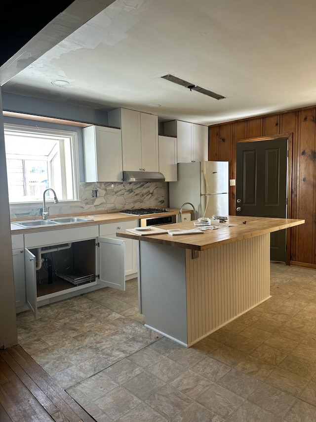 kitchen featuring wooden counters, a kitchen island, sink, white refrigerator, and white cabinetry