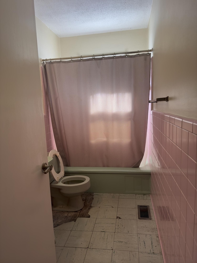 bathroom featuring shower / tub combo, a textured ceiling, toilet, and tile walls