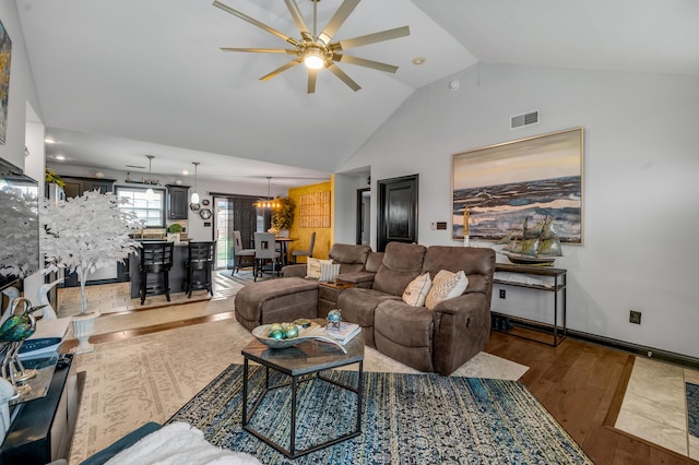 living room with ceiling fan with notable chandelier, dark wood-type flooring, and vaulted ceiling