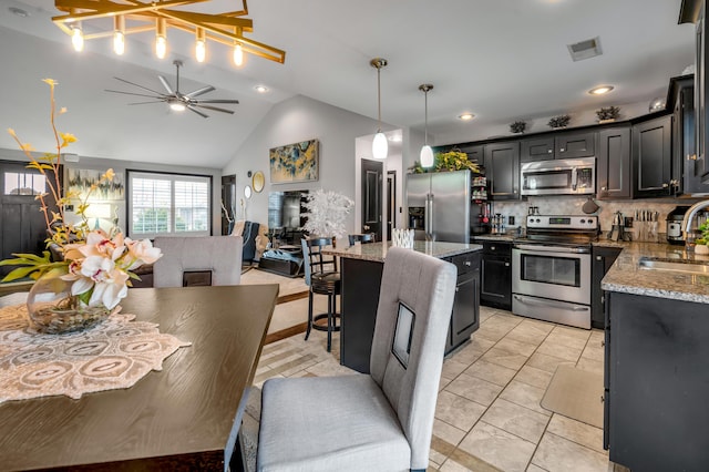 kitchen featuring light stone countertops, a center island, ceiling fan, stainless steel appliances, and backsplash