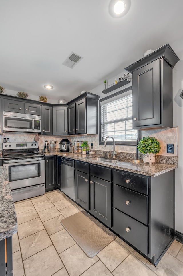 kitchen with backsplash, stone counters, sink, light tile patterned floors, and appliances with stainless steel finishes