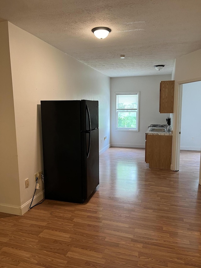 kitchen with black refrigerator, a textured ceiling, and hardwood / wood-style flooring