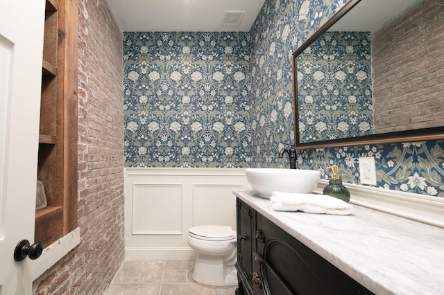 bathroom with tile patterned flooring, vanity, toilet, and brick wall