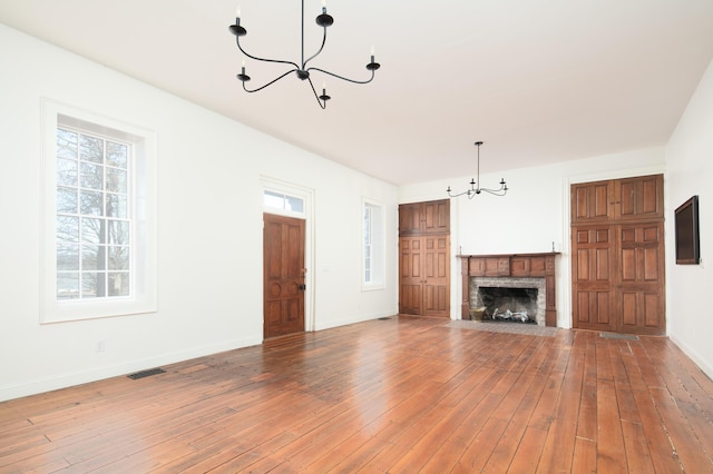 unfurnished living room with a fireplace, an inviting chandelier, and hardwood / wood-style flooring