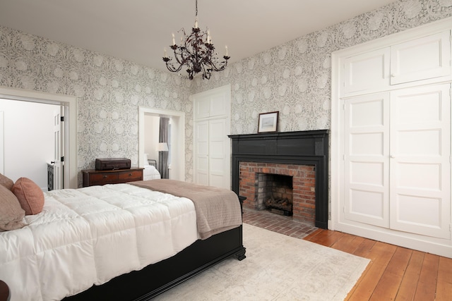 bedroom featuring hardwood / wood-style flooring, a notable chandelier, and a brick fireplace