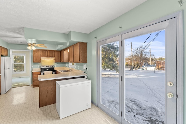 kitchen with kitchen peninsula, white fridge, ceiling fan, stainless steel range with electric stovetop, and sink