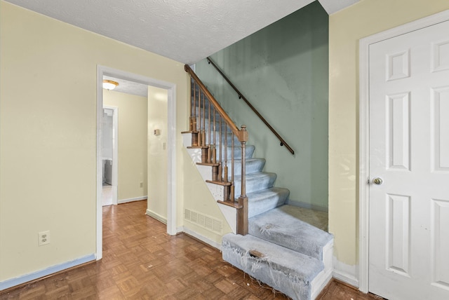 stairs featuring a textured ceiling and parquet flooring