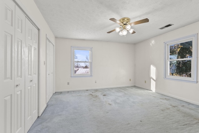 unfurnished bedroom featuring light carpet, ceiling fan, a textured ceiling, and multiple closets