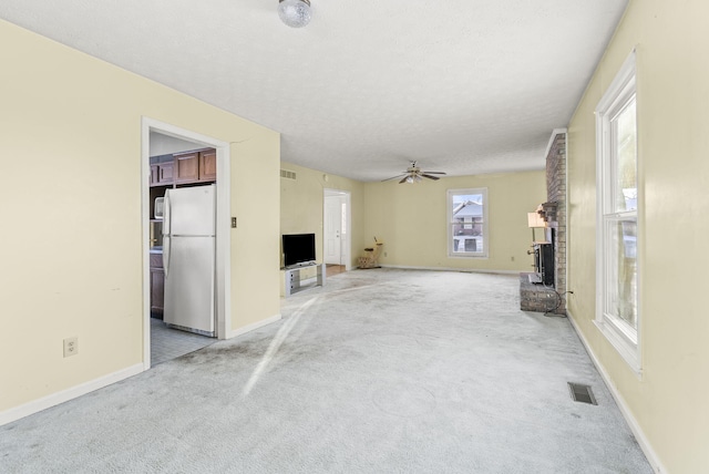 unfurnished living room with a fireplace, a textured ceiling, ceiling fan, and light carpet