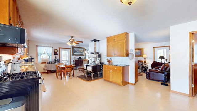 kitchen with tasteful backsplash, a wood stove, stainless steel range with gas stovetop, and ceiling fan