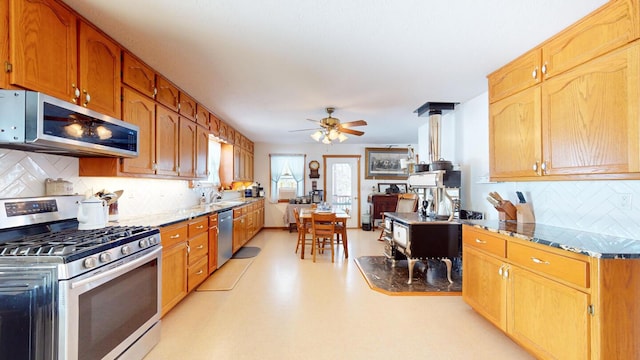 kitchen with sink, ceiling fan, stainless steel appliances, decorative backsplash, and a wood stove