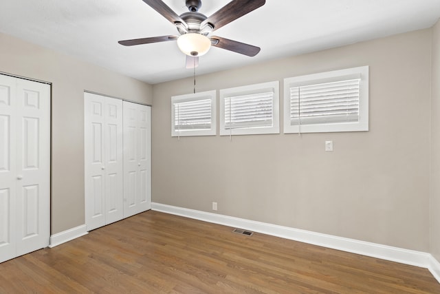 unfurnished bedroom featuring multiple closets, ceiling fan, and hardwood / wood-style floors