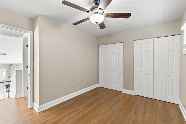 unfurnished bedroom with multiple closets, ceiling fan, and hardwood / wood-style floors