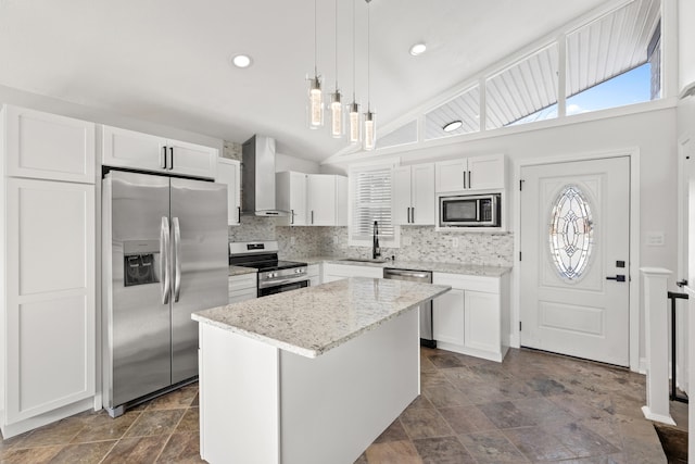 kitchen featuring wall chimney exhaust hood, stainless steel appliances, pendant lighting, a center island, and white cabinetry