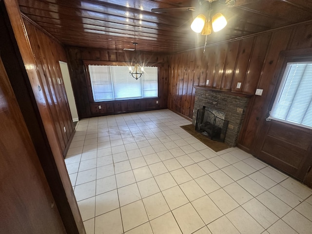 unfurnished living room featuring wood ceiling, wooden walls, a stone fireplace, and light tile patterned floors