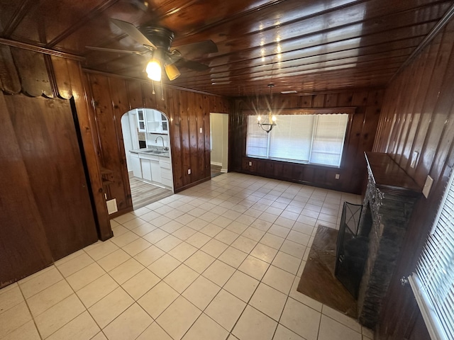 interior space with light tile patterned floors, sink, ceiling fan with notable chandelier, wooden ceiling, and wood walls