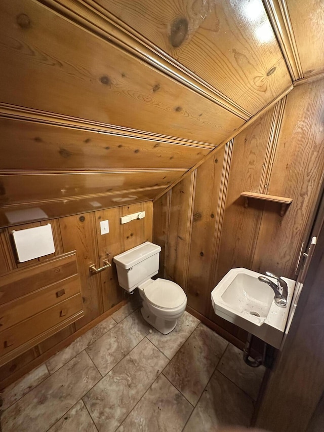 bathroom featuring toilet, wood ceiling, a sink, wooden walls, and lofted ceiling