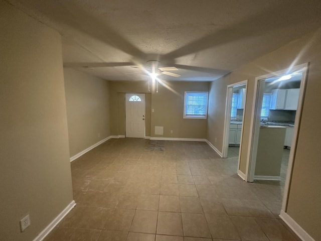 unfurnished room with a textured ceiling, baseboards, tile patterned floors, and a ceiling fan