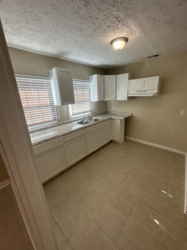 kitchen with baseboards, a textured ceiling, a sink, visible vents, and white cabinets