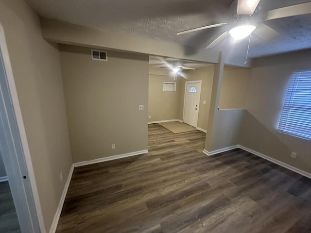 below grade area with dark wood finished floors, baseboards, visible vents, and ceiling fan