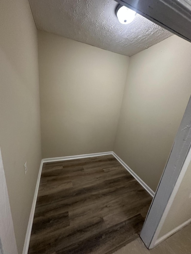 unfurnished room featuring dark wood-type flooring, a textured ceiling, and baseboards