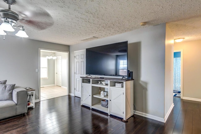 living room with ceiling fan with notable chandelier, a textured ceiling, and dark wood-type flooring