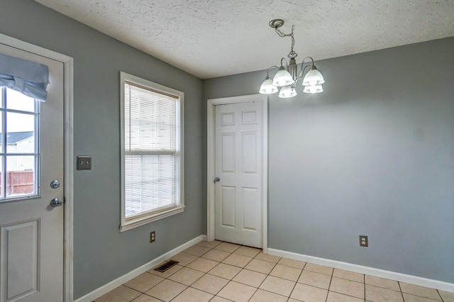 unfurnished dining area with light tile patterned floors, a textured ceiling, and an inviting chandelier