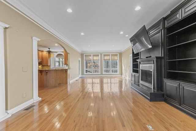 unfurnished living room with ceiling fan, ornamental molding, light hardwood / wood-style flooring, and decorative columns