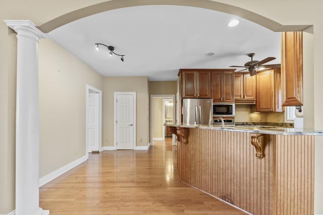 kitchen featuring a kitchen bar, kitchen peninsula, ornate columns, black microwave, and stainless steel refrigerator