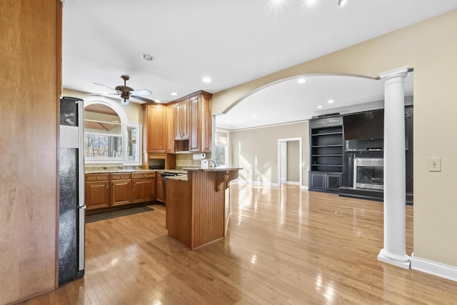 kitchen featuring a kitchen breakfast bar, ceiling fan, light wood-type flooring, a fireplace, and decorative columns