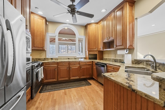 kitchen featuring appliances with stainless steel finishes, light stone counters, ceiling fan, sink, and light hardwood / wood-style floors