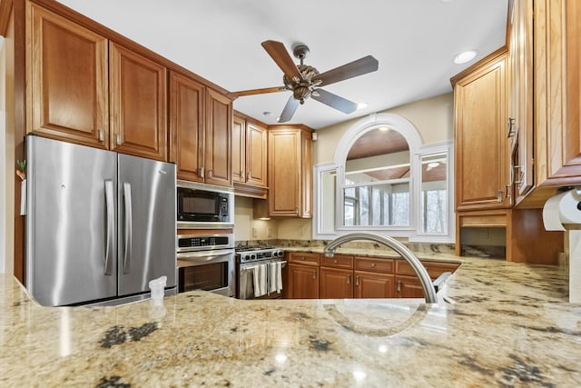 kitchen with stainless steel appliances, light stone counters, and ceiling fan