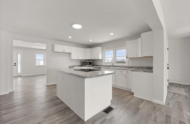 kitchen featuring sink, black electric stovetop, light hardwood / wood-style floors, white cabinets, and a kitchen island